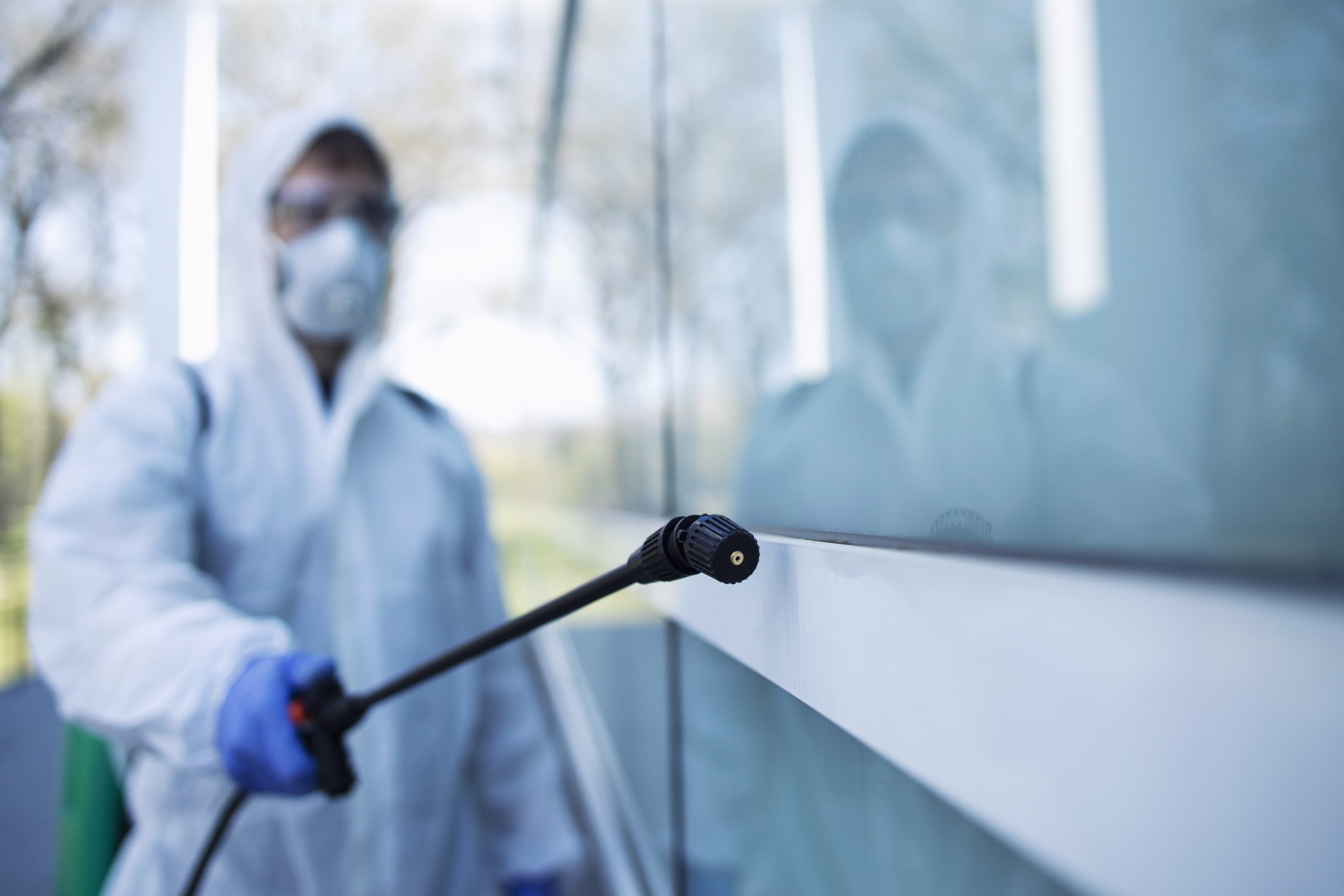 Person in white chemical protection suit doing disinfection of public areas to stop spreading highly contagious corona virus.